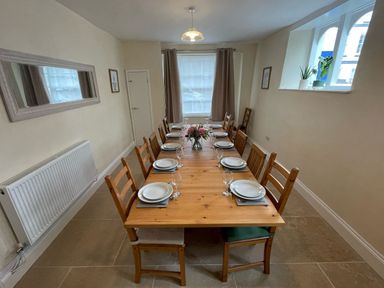 A dining room with a wooden table set with plates and glasses chairs around the table and potted plants on the windowsill at The Hame in Monmouth