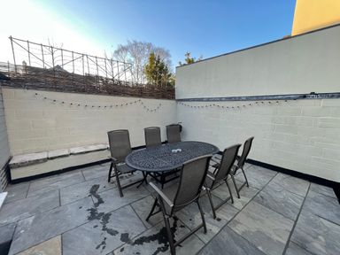 An outdoor patio with a black metal table and six chairs with string lights on the walls at The Hame in Monmouth