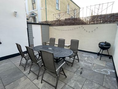 An outdoor patio with six chairs around a metal table a barbecue and a shed at The Hame in Monmouth