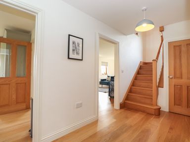 An entry hallway with wooden stairs doors and a framed picture on the wall at Whin Hill Cottage in Craster