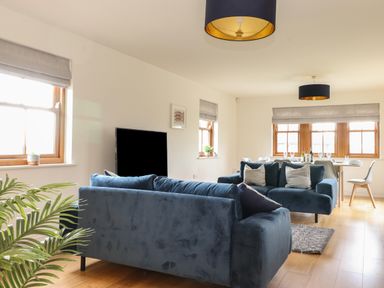 A living room with two blue sofas a television and a dining table with chairs at Whin Hill Cottage in Craster