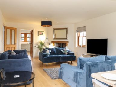 A living room with blue sofas a television a wooden floor and a doorway leading to a kitchen at Whin Hill Cottage in Craster