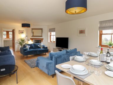 A living room with blue sofas a dining table set with plates glasses and wine bottles at Whin Hill Cottage in Craster