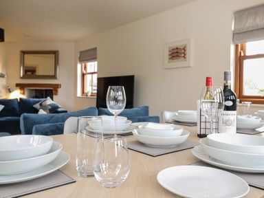 A dining table set with white dishes and glassware in a living room with blue sofas and a fireplace at Whin Hill Cottage in Craster