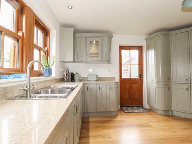 A kitchen with cabinets a double sink a wooden door and wooden framed windows at Whin Hill Cottage in Craster