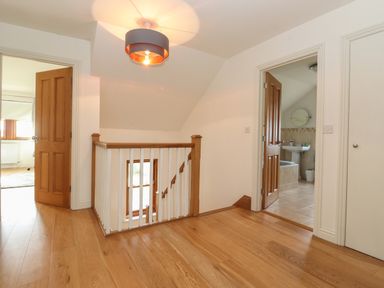 A hallway with wooden floors and railing with open doors leading to a bathroom and another room at Whin Hill Cottage in Craster