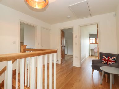 A hallway with wooden floor a railing gray chair beside a small round table and doors leading to other rooms at Whin Hill Cottage in Craster