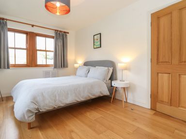 A bedroom with a bed bedside tables lamps wooden floor and wooden door at Whin Hill Cottage Craster