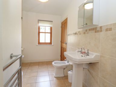A bathroom with a pedestal sink bidet toilet a wooden door and a window at Whin Hill Cottage in Craster