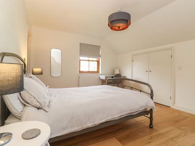 A bedroom with a metal bed frame a bedside table two lamps a window and a desk with a chair at Whin Hill Cottage in Craster