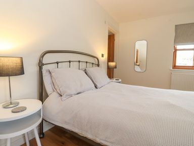 A bedroom with a double bed, bedside tables with lamps, a wall mirror, and a window at Whin Hill Cottage in Craster