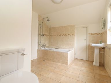 A bathroom with a toilet sink bathtub shower and a small door at Whin Hill Cottage in Craster