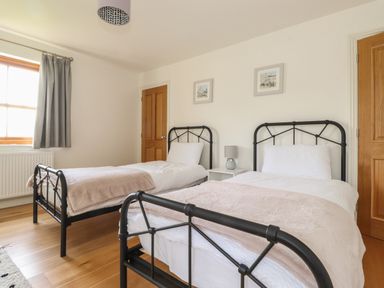 A bedroom with two single metal beds a window with gray curtains and wooden doors at Whin Hill Cottage in Craster