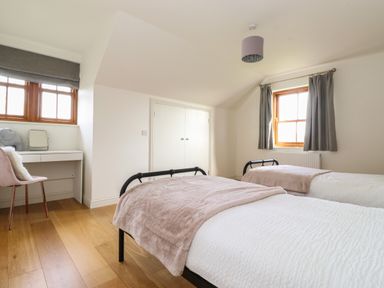 A bedroom with two single beds a desk with a chair and windows with curtains at Whin Hill Cottage in Craster