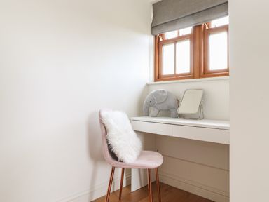 A workspace with a white desk a pink chair with a white cushion a small mirror and a stuffed elephant near a window at Whin Hill Cottage in Craster