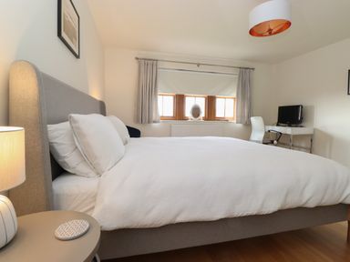 A bedroom with a bed side table lamp and desk with chair and television at Whin Hill Cottage in Craster