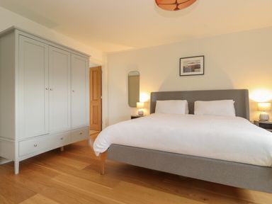 A bedroom with a double bed two bedside tables with lamps a wardrobe and a framed picture at Whin Hill Cottage in Craster