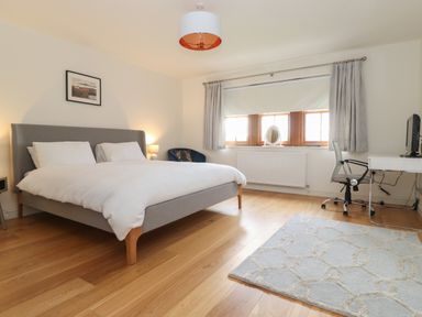 A bedroom with a bed a desk and chair a window with curtains and a rug on a wooden floor at Whin Hill Cottage in Craster