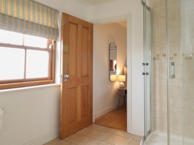 A bathroom with tiled floor window with striped blind wooden door and a glass shower enclosure at Whin Hill Cottage in Craster