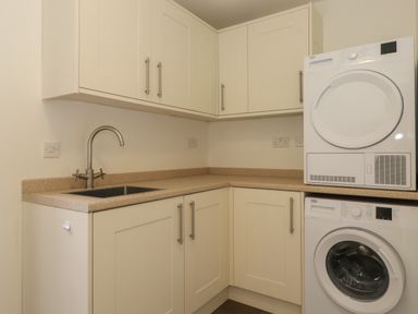 A laundry room with a washing machine dryer sink and cabinets at Whin Hill Cottage in Craster