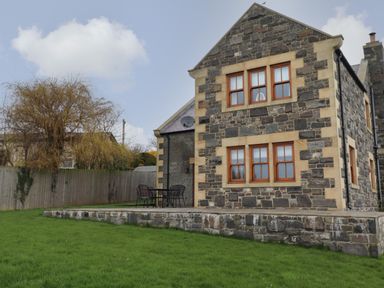A stone house with four wooden framed windows and a patio with a table and chairs on a grass lawn at Whin Hill Cottage in Craster