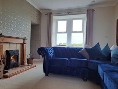 A living room with a blue sectional sofa and a fireplace near a window at Bogrie Cottage in Canonbie near Gretna Green