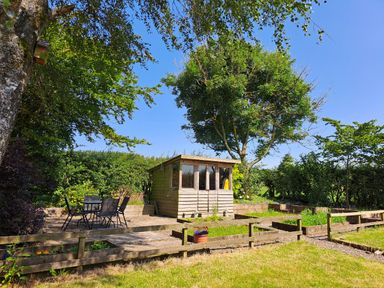 A garden with a wooden shed a table with four chairs and raised plant beds at Bogrie Cottage in Canonbie near Gretna Green