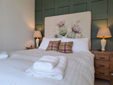 A bedroom with a double bed two bedside tables with lamps and folded towels on the bed at Bogrie Cottage in Canonbie near Gretna Green