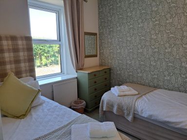 A bedroom with two beds a window with curtains a green chest of drawers and a wall mirror at Bogrie Cottage Canonbie near Gretna Green