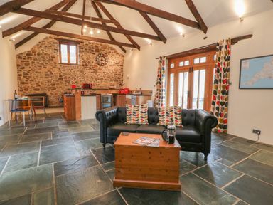 A living area with a black sofa and wooden coffee table near a kitchen and stone wall at The Threshing Barn in Highampton