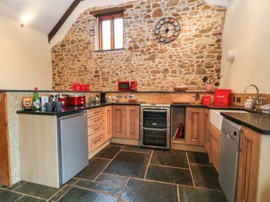 A kitchen with stone walls wooden cabinets and black countertops at The Threshing Barn in Highampton