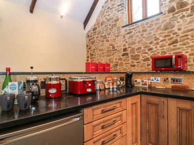 A kitchen countertop with red appliances and containers on black surface and wooden cabinets below at The Threshing Barn in Highampton