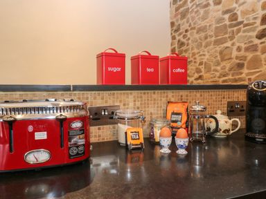 A kitchen counter with a red toaster red containers labeled sugar tea coffee jars of tea and coffee two eggs in egg cups a teapot and a coffee machine at The Threshing Barn in Highampton