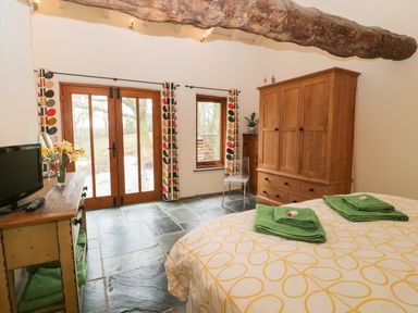 A bedroom with wooden wardrobe glass door and patterned curtains at The Threshing Barn in Highampton
