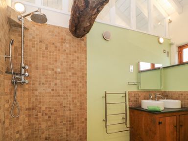 A bathroom with a tiled shower area a wooden vanity with two sinks and a mirror at The Threshing Barn in Highampton