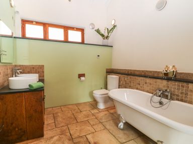 A bathroom with a clawfoot bathtub toilet dual sinks and a plant on a shelf at The Threshing Barn in Highampton