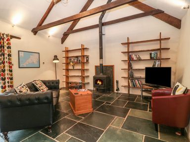 A living room with a black sofa red armchair wooden shelves fireplace and television at The Threshing Barn in Highampton