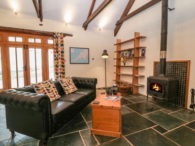 A living room with a black sofa and coffee table near a wood burning stove at The Threshing Barn in Highampton