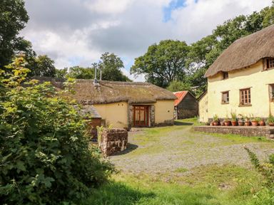 A rural scene with thatched cottages surrounded by trees and plants at The Threshing Barn in Highampton