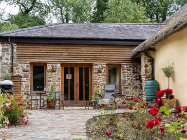 An outdoor patio with stone flooring chairs and a table in front of a stone and wood building at The Threshing Barn in Highampton