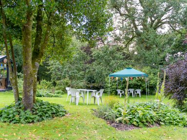 A garden with white plastic chairs and tables and a green canopy with buntings at The Threshing Barn in Highampton