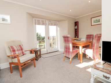 A dining area with a wooden table and four red plaid chairs next to double doors and an armchair with a red plaid cushion at Magnolia House in Dittisham