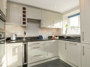 A kitchen with white cabinets black countertops a window with a blue blind and various kitchen items on the counter at Magnolia House in Dittisham