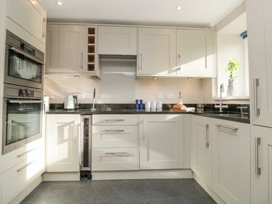 A kitchen with white cabinets a black countertop a built-in oven and microwave and a window with a flower vase at Magnolia House in Dittisham