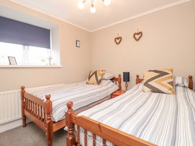 A bedroom with two single wooden beds with striped bedding and pillows a bedside table with a lamp and two heart decorations on the wall at Magnolia House in Dittisham
