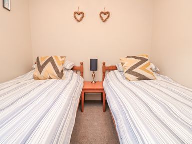 A bedroom with two single beds with striped bedding and patterned pillows a small wooden bedside table with a lamp and two heart-shaped wall decorations at Magnolia House in Dittisham