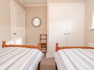 A bedroom with two single beds with striped bedding a wooden chair a round wall mirror a white door and a white double closet at Magnolia House in Dittisham