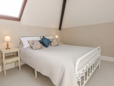A bedroom with a white metal bed frame a beige quilt and floral and blue pillows two bedside tables with lamps and a skylight window at Magnolia House in Dittisham