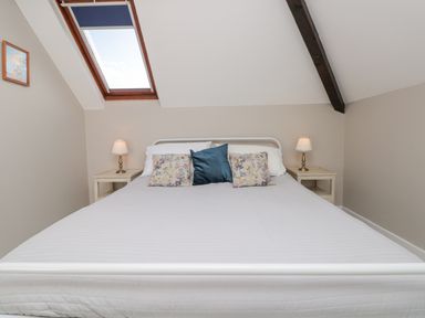 A bedroom with a double bed white bedding floral and blue pillows two bedside tables with lamps skylight window and slanted ceiling beam at Magnolia House in Dittisham