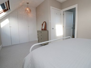 A bedroom with a white bed frame a dresser with a mirror built in wardrobes and two white doors at Magnolia House in Dittisham